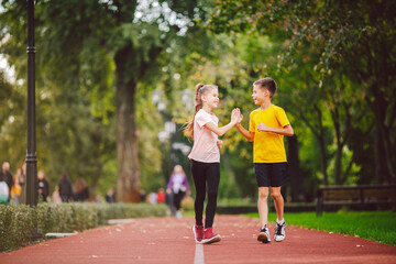 Couple of kids boy and girl doing cardio workout, jogging in park on jogging track red. Cute twins...