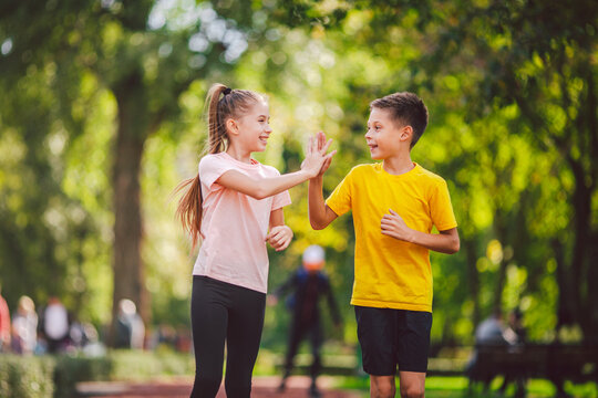 Sports and fitness in adolescence. Caucasian twins boy and girl run on the jogging track in the city park. Two children brother and sister for 10 years running on a rubberized outdoor treadmill