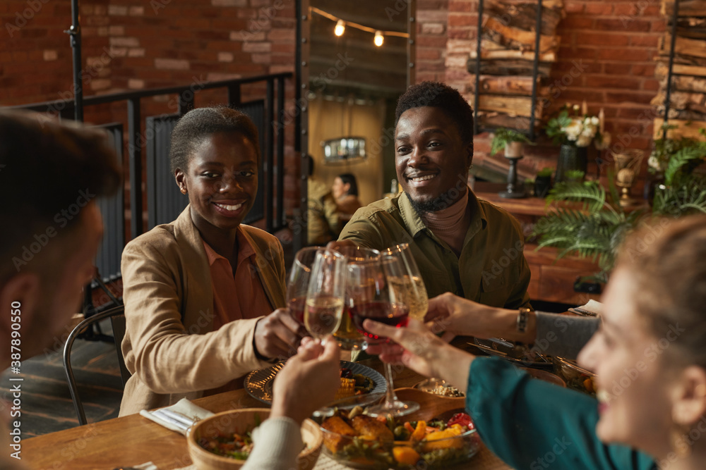 Wall mural portrait of young african-american couple clinking glasses while enjoying dinner party with friends 