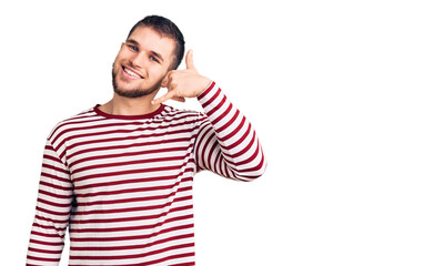 Fototapeta premium Young handsome man wearing striped sweater smiling doing phone gesture with hand and fingers like talking on the telephone. communicating concepts.