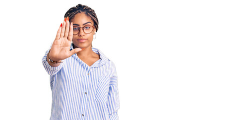 Fototapeta premium Young african american woman with braids wearing casual clothes and glasses doing stop sing with palm of the hand. warning expression with negative and serious gesture on the face.
