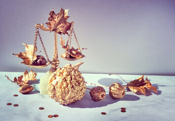 Minimalist Autumn background with gold weight scales, gold pumpkins, leaves, acorns and confetti.