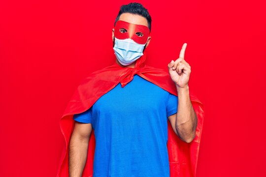 Young hispanic man wearing super hero costume and medical mask smiling happy pointing with hand and finger to the side