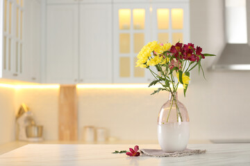 Vase with beautiful flowers on table in kitchen, space for text. Stylish element of interior design