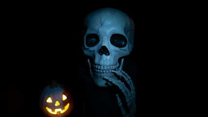 Skull with skeleton hand and white glowing pumpkin in the background for Halloween