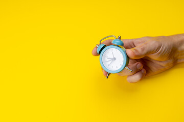 person holding old blue clock over yellow background. copy space. studio shot. time concept. schedule symbol