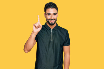 Young man with beard wearing sportswear showing and pointing up with finger number one while smiling confident and happy.