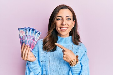 Young brunette woman holding hong kong 10 dollars banknotes smiling happy pointing with hand and finger