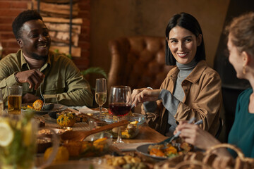 Multi-ethnic group of friends smiling happily while enjoying dinner party in cozy lighting