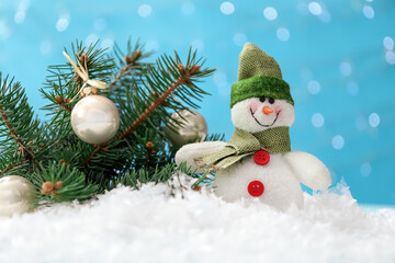 Fototapeta na wymiar Cute toy snowman and fir branch decorated with Christmas balls on snow against blurred background