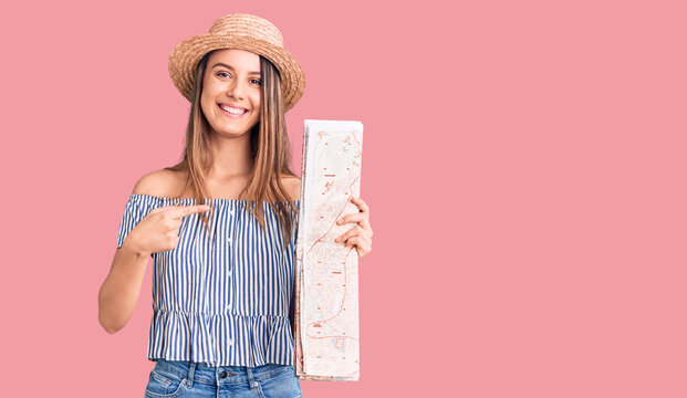 Young beautiful girl wearing hat holding city map smiling happy pointing with hand and finger