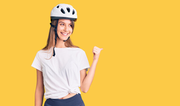 Young beautiful girl wearing bike helmet smiling with happy face looking and pointing to the side with thumb up.