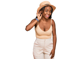 Young black woman wearing summer hat smiling with hand over ear listening an hearing to rumor or gossip. deafness concept.