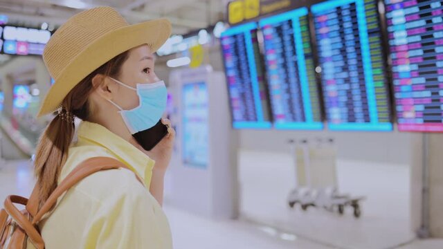 Asian woman calling on the phone looking for friend in in front fly schedule timetable in airport. concept of travel, appointment and travel safe new normal