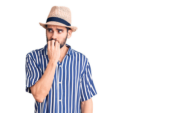 Young handsome man with beard wearing summer hat and striped shirt looking stressed and nervous with hands on mouth biting nails. anxiety problem.