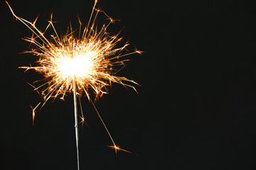 Bright burning sparkler on black background, closeup. Space for text