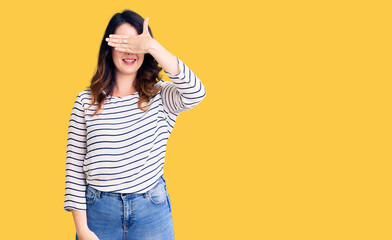 Beautiful young brunette woman wearing casual clothes and glasses smiling and laughing with hand on face covering eyes for surprise. blind concept.