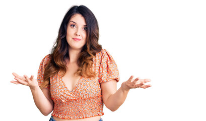 Beautiful young brunette woman wearing casual clothes clueless and confused expression with arms and hands raised. doubt concept.