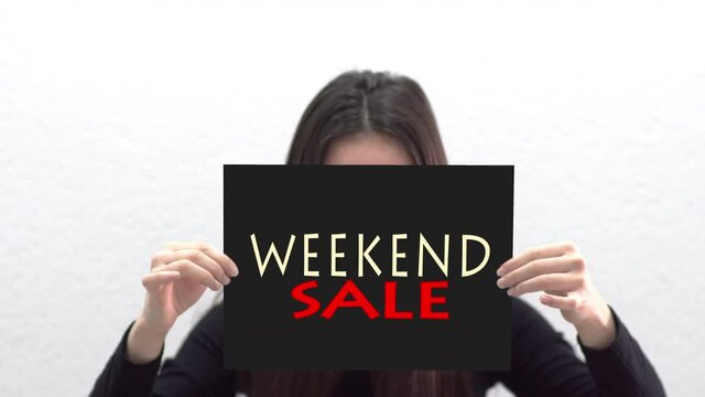 Conceptual message "Weekend Sale" on canvas frame label hold by beautiful girl smiling at camera
