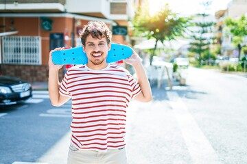 Young caucasian skater man smiling happy holding skate walking at street of city. © Krakenimages.com