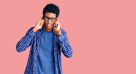 Young african american man wearing casual clothes and glasses covering ears with fingers with annoyed expression for the noise of loud music. deaf concept.