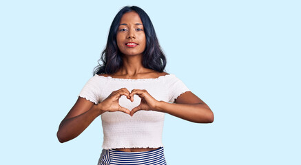 Young indian girl wearing casual clothes smiling in love showing heart symbol and shape with hands....