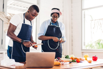 Portrait of love african american couple having fun cooking together and looking for recipe on Internet with laptop computer to prepare the yummy eating in kitchen at home