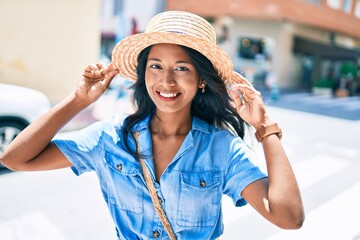 Young beautiful indian woman wearing summer hat smiling happy walking at the city.