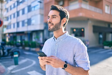 Young hispanic man smiling happy using smartphone at city.