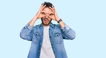 Young hispanic man wearing casual clothes doing ok gesture like binoculars sticking tongue out, eyes looking through fingers. crazy expression.