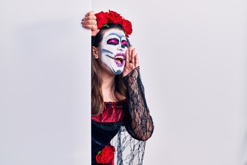 Young woman wearing day of the dead custome holding blank empty banner shouting and screaming loud to side with hand on mouth. communication concept.