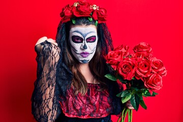 Young woman wearing day of the dead costume holding flowers annoyed and frustrated shouting with anger, yelling crazy with anger and hand raised