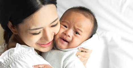 Portrait of enjoy happy love family asian mother playing with adorable little asian baby.Mom kiss with cute son moments good time in a white bedroom.Love of family concept