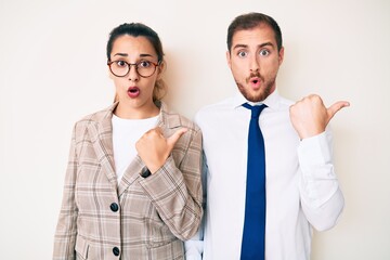 Beautiful couple wearing business clothes surprised pointing with hand finger to the side, open mouth amazed expression.