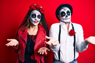 Couple wearing day of the dead costume over red clueless and confused with open arms, no idea concept.