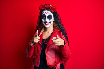 Woman wearing day of the dead costume over red pointing fingers to camera with happy and funny face. good energy and vibes.