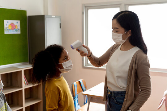 Group of diverse students in school building checked and scanned for temperature check. Elementary pupils are wearing a face mask and line up before entering into classroom. Covid-19 school reopen