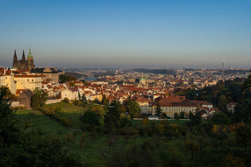 Fototapeta na wymiar the old St. Vitus Cathedral and Prague Castle and the nearby ones with trees and grass in autumn and a sky without clouds at sunset in the center of city