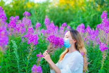 Fototapeta premium Girl in a medical mask sniffs a bouquet of flowers while walking in the park