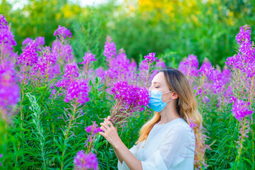Girl in a medical mask sniffs a bouquet of flowers while walking in the park