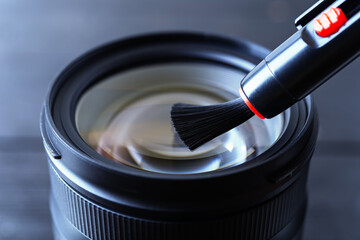 Sweeping dust from front lens using lens pen brush. Routine removal of dust and spots from photographic equipment. Maintenance close-up.