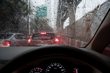 Raindrops run down on car windshield from inside view. Traffic jam during the heavy rain storm.