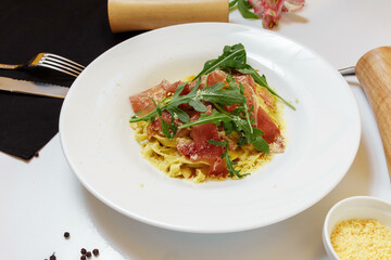 Tasty Italian pasta appetizer with basturma and fresh basil on top on a white table background with docures