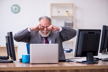 Old male boss sitting at desktop in the office