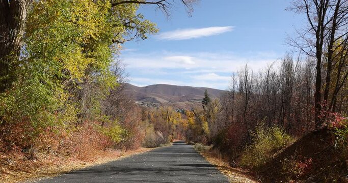 Mountain road scenic autumn leaves valley view 4K. Beautiful autumn fall colors along Wasatch Mountains. Valley landscape with road and colorful fall trees. Rural farming community road.
