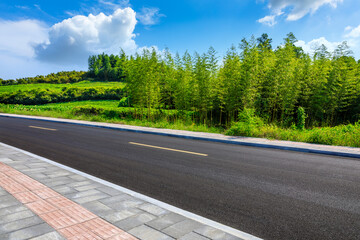 Fototapeta premium Asphalt road and green bamboo with mountain natural scenery in Hangzhou on a sunny day.
