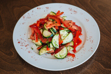 Classic salad with cucumbers and tomatoes sprinkled with dill. Diet food. On a white plate. Dish on a dark background.
