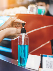 Hands of woman pressed blue alcohol gel bottle to prevent the spreading of the Coronavirus (Covid-19) before entrance to coffee shop. New normal lifestyle. Selective focus on alcohol gel bottle.