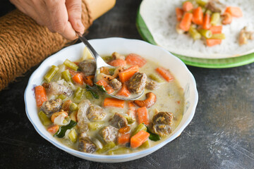 Mutton stew , chicken stew soup side dish for Appam , bread, Kerala breakfast food. Indian food. Christian Christmas food woman hand take spicy curry with coconut milk, meat, vegetables, Indian spices