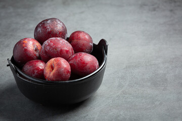 red plum put in black bowl on dark floor